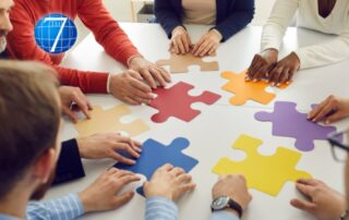 A diverse team of professionals collaboratively working to assemble a large puzzle on a table, symbolizing teamwork, problem-solving, and the collective effort required to navigate through organizational change and transitions. The image reflects the importance of leadership in guiding and supporting a team as they piece together the complex aspects of change management.