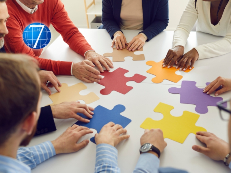 A diverse team of professionals collaboratively working to assemble a large puzzle on a table, symbolizing teamwork, problem-solving, and the collective effort required to navigate through organizational change and transitions. The image reflects the importance of leadership in guiding and supporting a team as they piece together the complex aspects of change management.