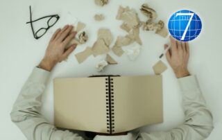 An image depicting decision fatigue: a person overwhelmed at a desk with their head buried in an open notebook, surrounded by crumpled paper and a pair of glasses, symbolizing mental exhaustion from decision-making.