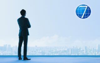 A professional-looking individual stands confidently in front of a large window overlooking a city skyline, symbolizing emotional agility in leadership and the ability to navigate challenges with clarity and composure.
