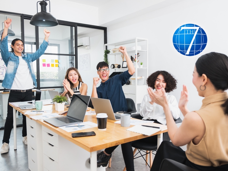 A cheerful team celebrating and collaborating in a modern office, demonstrating playfulness in leadership through an engaging and fun work environment.